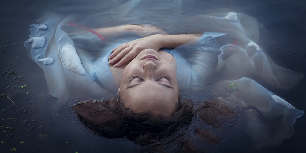 Young beautiful drowned woman in blue dress lying in the water